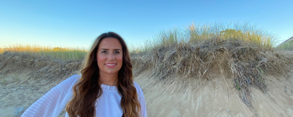 Tara Gans, parenting coach for moms, standing on a sand dune, smiling and looking confident.